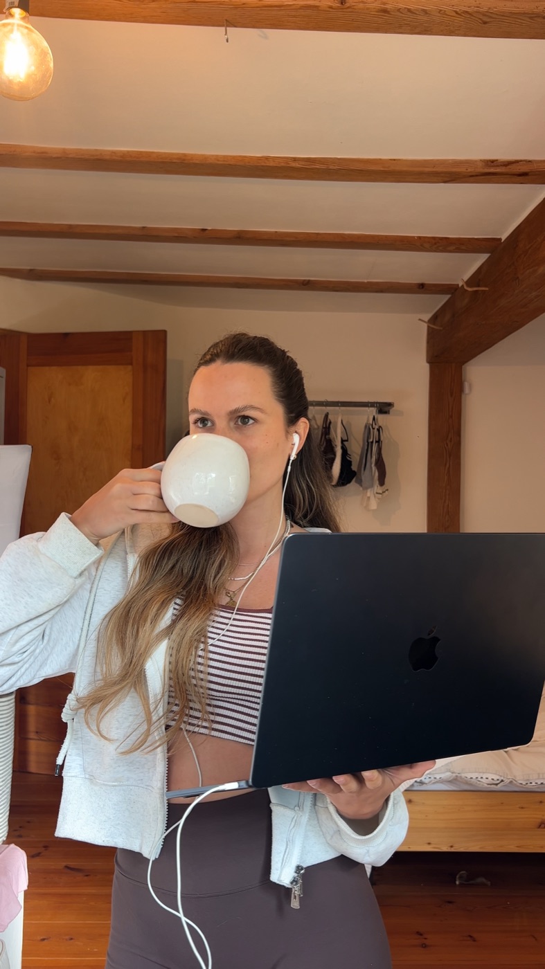 Yule sipping from a big mug while holding her open laptop